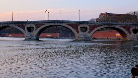 Young-couple-enjoying-sunset-in-front-of-"Pont-Neuf"-in-Toulouse,-France