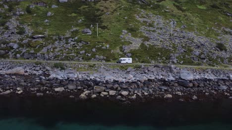 Flying-over-the-ocean-looking-at-a-coastal-road-with-a-campervan-driving