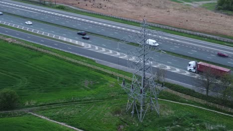 Fahrzeuge-Auf-Der-Autobahn-M62,-Vorbei-Am-Pylonturm-Auf-Landwirtschaftlichen-Feldern,-Luftaufnahme,-Umlaufbahn-Rechts