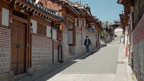 Man-in-protective-mask-walking-down-the-traditional-street-of-Bukchon-Hanok-Village-during-covid-19-pandemic-in-Seoul,-South-Korea