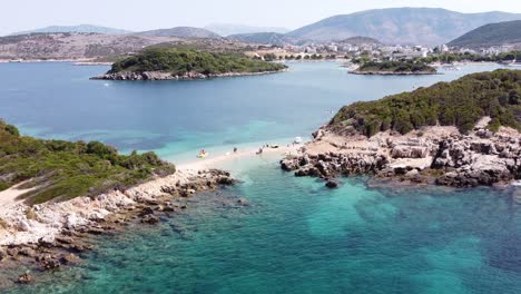 People-Relax-at-Small-Beach-and-Sand-Strip-at-Ksamil-Islands,-Albania---Reversing-Aerial