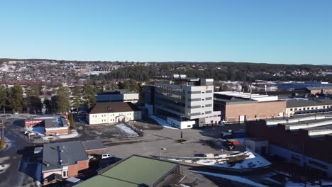 Distant-rotating-aerial-view-of-Kongsberg-Defence-and-Aerospace-headquarter-with-logo---Technology-company---Manufacturing-buildings-to-the-right-and-Kongsberg-city-in-background