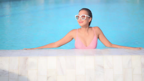 An-attractive-woman-fresh-from-swimming-leans-along-the-edge-of-a-swimming-pool