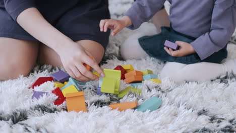 Slow-motion-footage-of-a-Mother-and-Daughter-building-toy-blocks-on-a-white-carpet