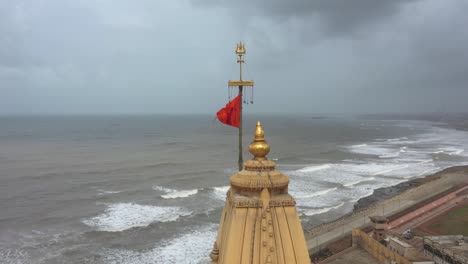 Luftaufnahme-Des-Kopfes-Von-Somnath-Mandir-Mit-Hinduistischer-Flagge,-Die-Im-Windigen,-Nebligen-Wetter-Weht