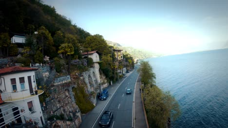 FPV-drone-shot-over-the-water-along-the-Swiss-and-Italian-coastline,-flying-around-boats,-alongside-cars,-over-trees,-over-water-6