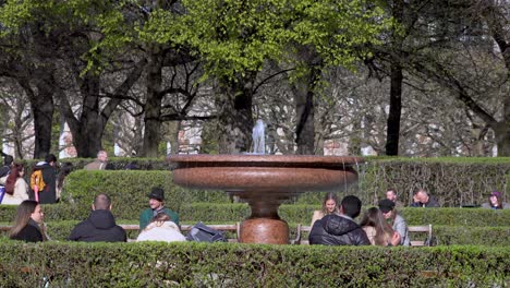 People-sitting-around-a-fountain-at-the-Hofgarten-in-Munich,-Bavaria,-Germany-enjoying-a-nice-and-warm-spring-day