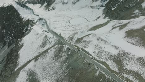 Vista-Aérea-De-Un-Todoterreno-Estacionado-En-Una-Desolada-Carretera-Invernal-Junto-Al-Paisaje-Cubierto-De-Nieve-En-La-Parte-Superior-De-Hunza