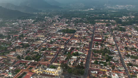 Fast-aerial-hyperlapse-zooming-in-on-the-Santa-Catalina-Arch-in-Antigua,-Guatemala-with-volcano-and-clouds-in-background