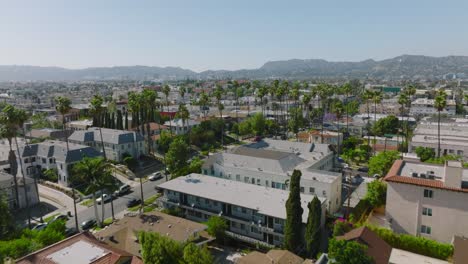 Flying-Over-a-Los-Angeles-Neighborhood-on-a-Sunny-Day,-Drone-Shot-Overlooking-Rooftops-with-Los-Angeles-Skyline-on-Horizon
