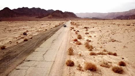 Passenger-car-drives-left-handed-fast-away-on-the-torn-dry-dirt-road-between-the-red-canyon-in-the-dry-Timna-Park-in-the-Negev-Desert-in-southern-Israel-on-a-sunny-day