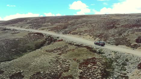Aerial-drone-of-a-red-suv-driving-up-a-hill-slowly-on-a-dirt-road-path-in-the-high-altitude-alpine-plain-and-mountains-of-Deosai-National-Park-located-between-Skardu-and-Astore-Valley-in-Pakistan