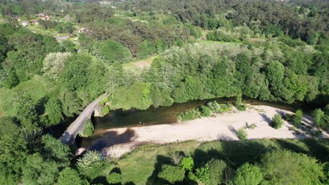 Aerial-drone-forward-moving-shot-flying-over-a-medieval-bridge-Das-Partidas-placed-over-the-river-Tea,-at-the-outskirts-of-the-town-of-Ponteareas,-Spain