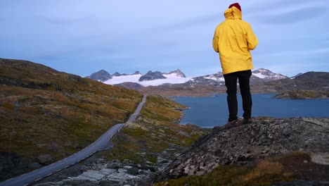 Man-in-a-yellow-rain-coat-in-front-of-impressive-landscape-of-Norway