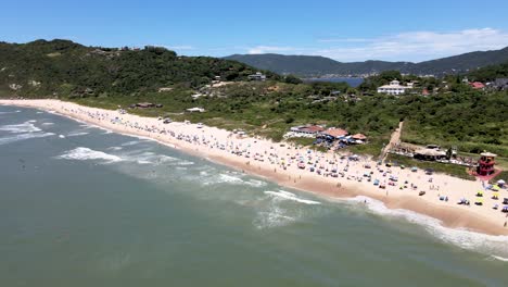Aerial-drone-view-of-tropical-tourist-beach-with-people-enjoying-the-sea-and-the-sand-umbrella-on-the-beach-mountains-in-the-background-and-lagoon-in-background