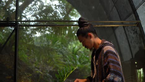 Asian-man-in-hipster-clothing-lighting-a-candle-with-forest-in-background,-camera-tilting-down