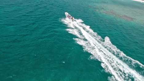 Speedboat-with-tourists-on-board-navigating-along-Playa-Ensenada-beach-leaving-white-wake,-Dominican-Republic