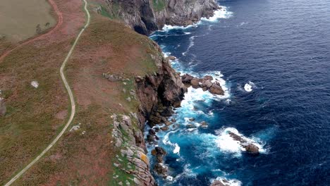 Aerial-bird's-eye-shot-of-narrow-pathway-along-paper-cliffs-in-the-area-of-Morás,-Xove,-Lugo,-Galicia,-Spain-during-evening-time