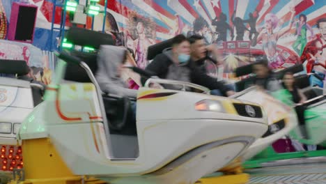 Group-waiting-as-people-happily-ride-inside-dizzy-spinning-cars-at-Balvarian-Spring-Fest-festival-at-Stuttgart,-Germany,-Europe-at-sunset,-panning-view-angle