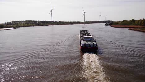 Vista-Aérea-De-Dolly-A-Lo-Largo-De-La-Popa-Del-Barco-Cisterna-De-Motor-Da-Vinci-Navegando-A-Lo-Largo-De-Oude-Maas-Con-Una-Fila-De-Turbinas-Eólicas-Vistas-En-Segundo-Plano.