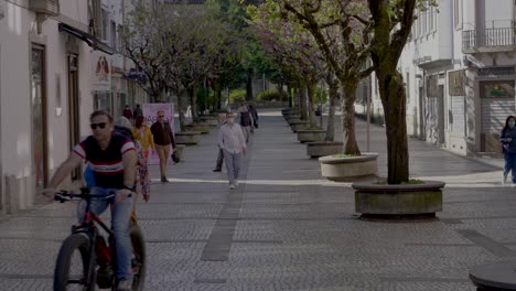 Man-cycling-between-pedestrians,-beautiful-Portuguese-pavement,-Braga,-Portugal