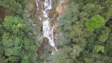 Low-aerial-slowly-ascends-steep-lush-green-jungle-waterfall-in-Laos