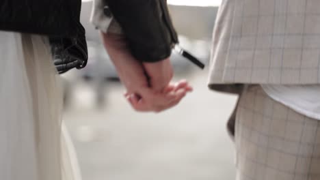 Close-up-shot-of-hands-of-retro-styled-wedding-couple-running-together-through-the-streets