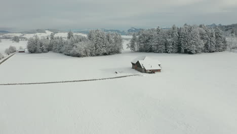 Aerial-of-small-farmhouse-in-snow-covered-winter-landscape