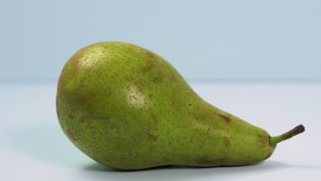 Fresh-big-green-pear-rotates-slowly-on-a-light-blue-background,-healthy-food-concept,-close-up-shot,-camera-rotate-right