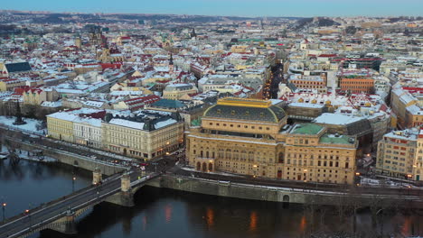 Aerial-view-of-Prague-cityscape-at-winter,-historic-buildings-by-river,-old-town-and-snow-capped-buildings,-Czech-Republic,-cinematic-drone-shot