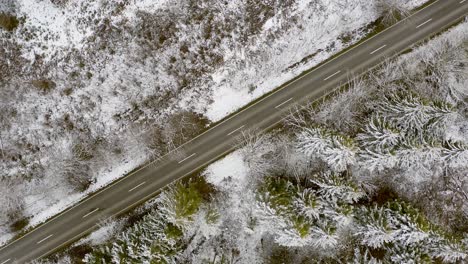Diagonal-directed-winter-road-straight-from-above-in-a-winter-forest-with-a-driving-car-directly-from-above