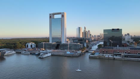 Aerial-dolly-in-of-boats-in-Puerto-Madero-docks-with-window-glass-skyscrapers-at-golden-hour,-Buenos-Aires