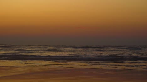 Magischer-Blick-Auf-Den-Strand-Während-Der-Goldenen-Stunde-Mit-Wellen,-Die-Unter-Orangefarbenem-Himmel-Auf-Die-Küste-Treffen