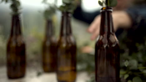Hands-arranging-beer-bottle-centerpieces-for-a-wedding,-close-up-forward-shot