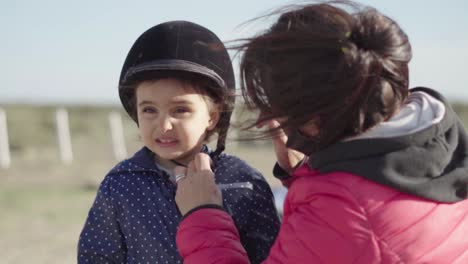 Mamá-Arregla-El-Casco-De-Su-Hija-Para-El-Paseo-A-Caballo