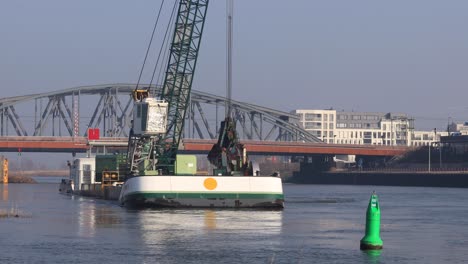 Dredging-ship-in-front-of-a-draw-bridge-clearing-the-waterway-of-river-IJssel-for-ships-passing-the-draw-bridge-corridor-at-the-IJsselkade-cityscape-boulevard