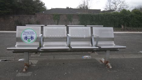 Close-up-of-a-coronavirus-sign-with-litter-on-a-metal-seat-at-a-quiet-train-station