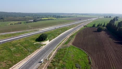 aerial,-almost-static,-forward-drone-shot-of-two-highways,-surrounded-by-fields,-green-grass,-trees,hills-and-blue-sky,-on-a-beautiful-sunny-day