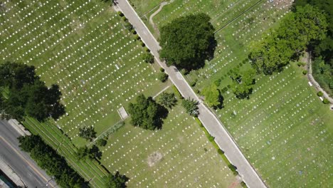 Aerial-view-of-a-cemetery-with-green-grass-and-cars-moving-on-a-nearby-highway
