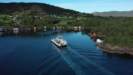 Electric-ferry-Ytteroyningen-soon-to-arrive-at-Utbjoa-ferry-pier-Norway---Aerial-crossing-behind-vessel-with-lush-green-landscape-background