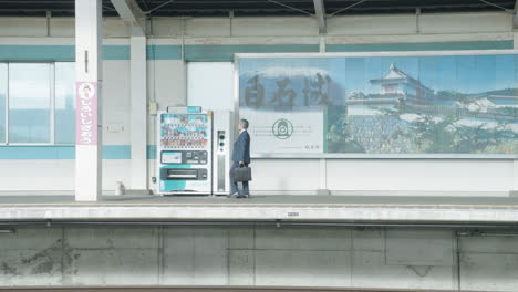 Empresario-Japonés-Caminando-Hacia-La-Máquina-Expendedora-En-La-Plataforma-De-La-Estación-De-Tren-De-Sendai,-Japón