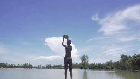 Junge-Spielt-Mit-Einem-Fußball-Vor-Einem-Fluss-In-Einem-Dorf-In-Bangladesch