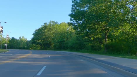 POV-while-driving-on-a-tree-lined-boulevard-in-a-Midwestern-college-town-past-parking-lots-for-the-University-of-Iowa,-main-campus-is-visible-in-the-distance