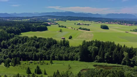 Aerial,-flying-smooth-to-the-right-by-showing-the-idyllic-landscape-in-southern-bavaria-in-the-alps-mountain-range-with-green-meadows-and-little-houses-and-villages---wonderful-nature-panning-shot