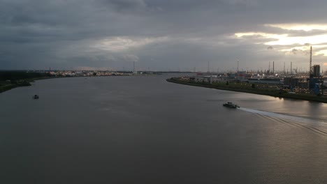Small-boat-sailing-away-near-industrial-buildings-on-Antwerp-harbor-during-stormy-sunset