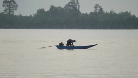 A-Thai-fisherman-cautiously-crawling-along-the-deck-of-a-fishing-boat,-crouched-on-his-haunches-as-he-starts-to-prepare-his-net-to-begin-fishing-on-a-beautiful-morning,-Chanthaburi-River,-Thailand