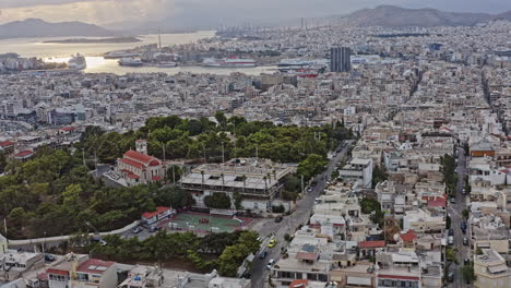 Pireas-Greece-Aerial-v10-low-level,-fly-around-kastella-hilltop-area-capturing-open-air-veakeio-theater-and-populated-downtown-cityscape-and-beautiful-main-port-in-the-background---September-2021