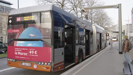 Electric-bus-charging-battery-at-the-bus-stop-while-passengers-stepping-in-the-vehicule
