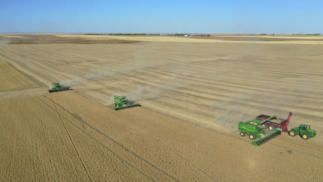 Aerial-zoom-out-above-three-combines-harvesting-wheat-in-Saskatchewan,-Canada