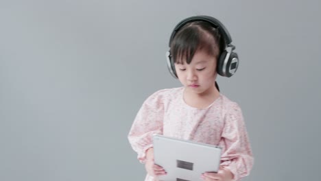 Kleines-Asiatisches-Mädchen-Mit-Kopfhörer-Genießt-Es,-Videos-Online-Auf-Dem-Tablet-Anzusehen-Und-Fröhlich-Zu-Tanzen
